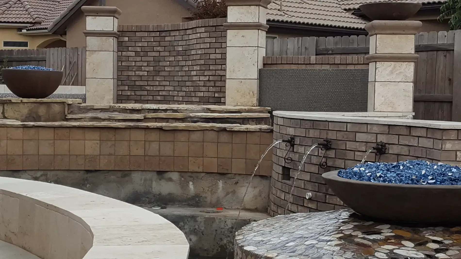 Stone backyard with a built-in fire bowl and blue decorative glass on a raised patio wall