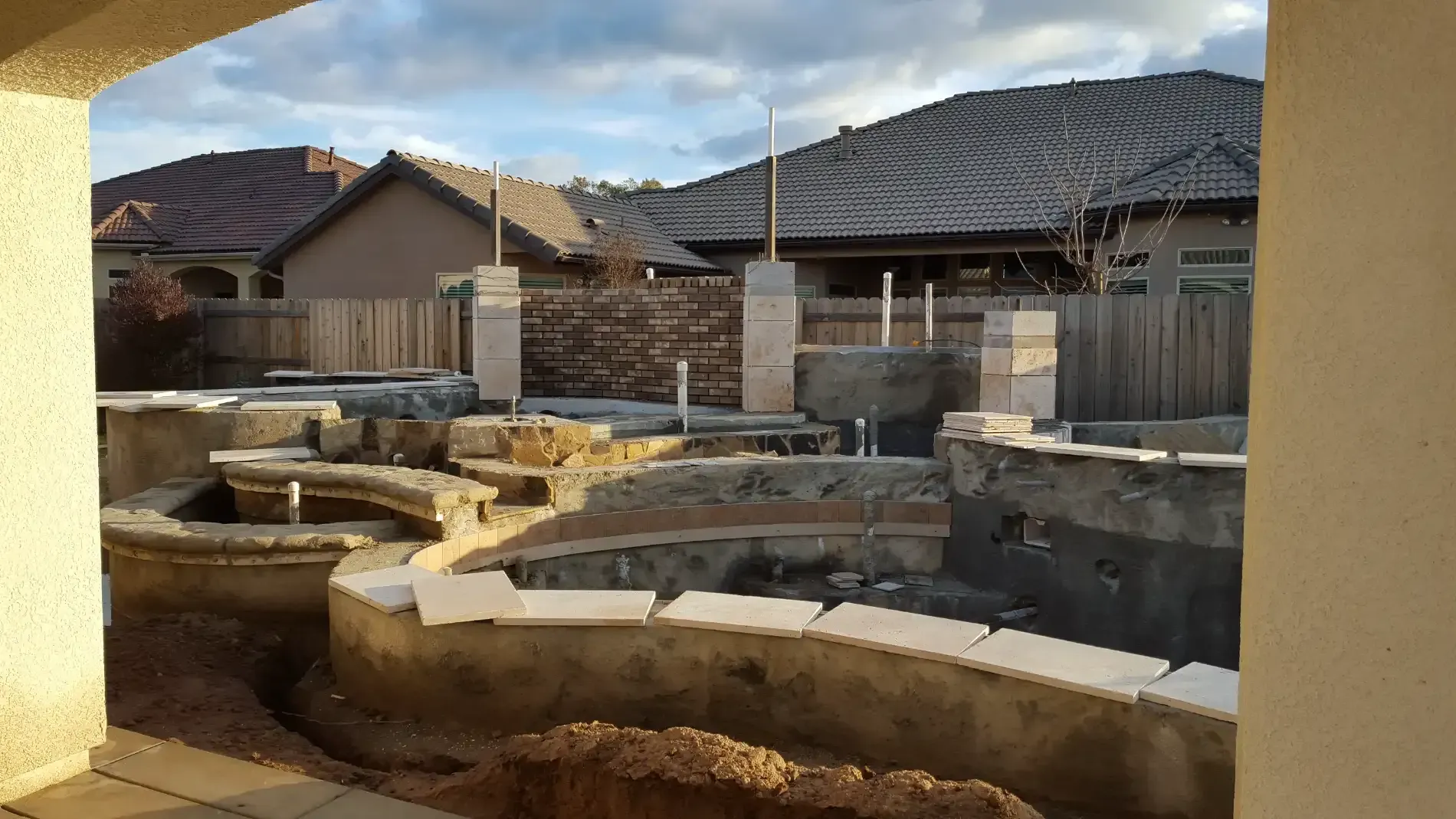 Backyard with stone foundation walls under construction beside suburban houses and a cloudy sky
