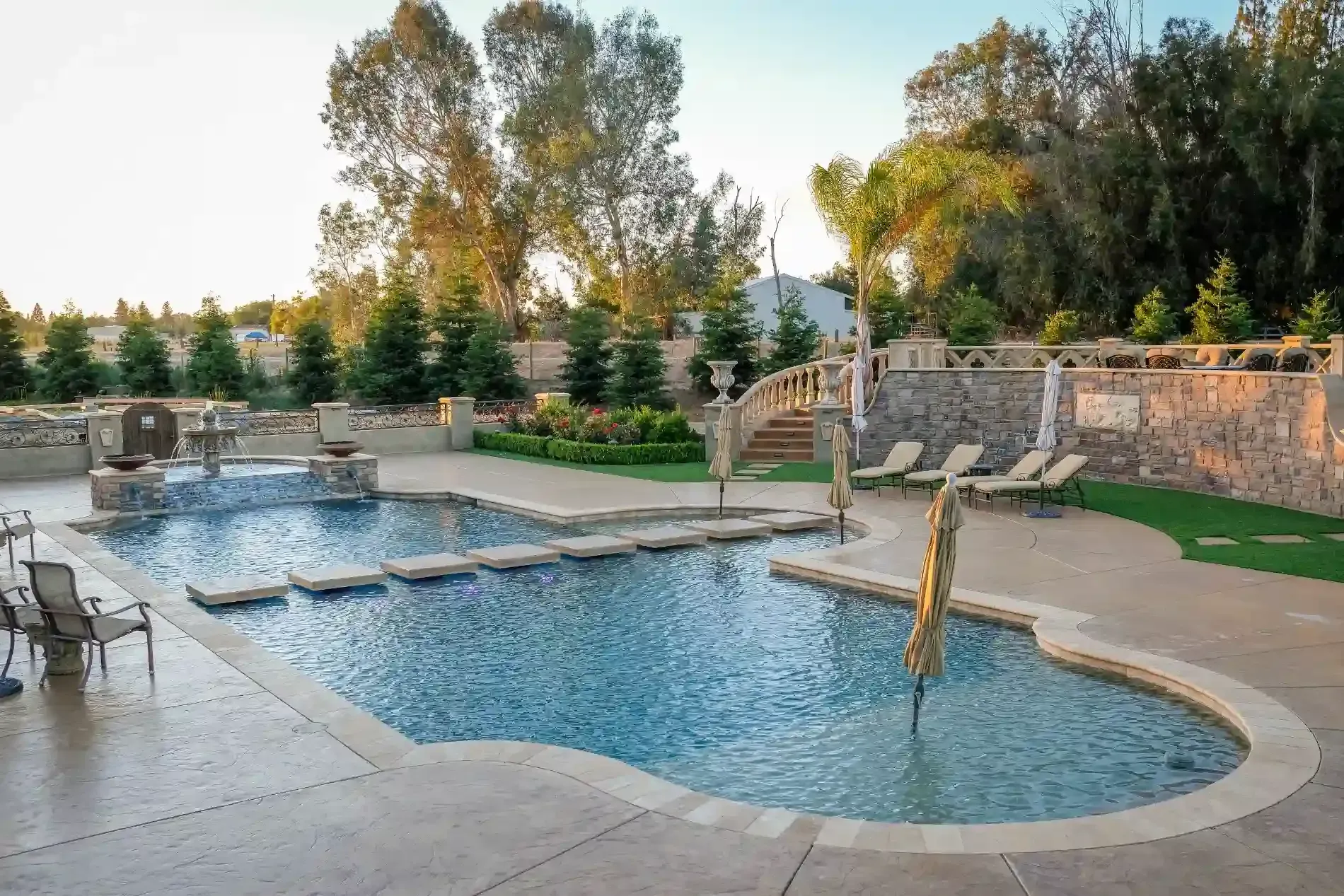 Backyard pool with stone patio, small waterfall, and landscaped garden at sunset