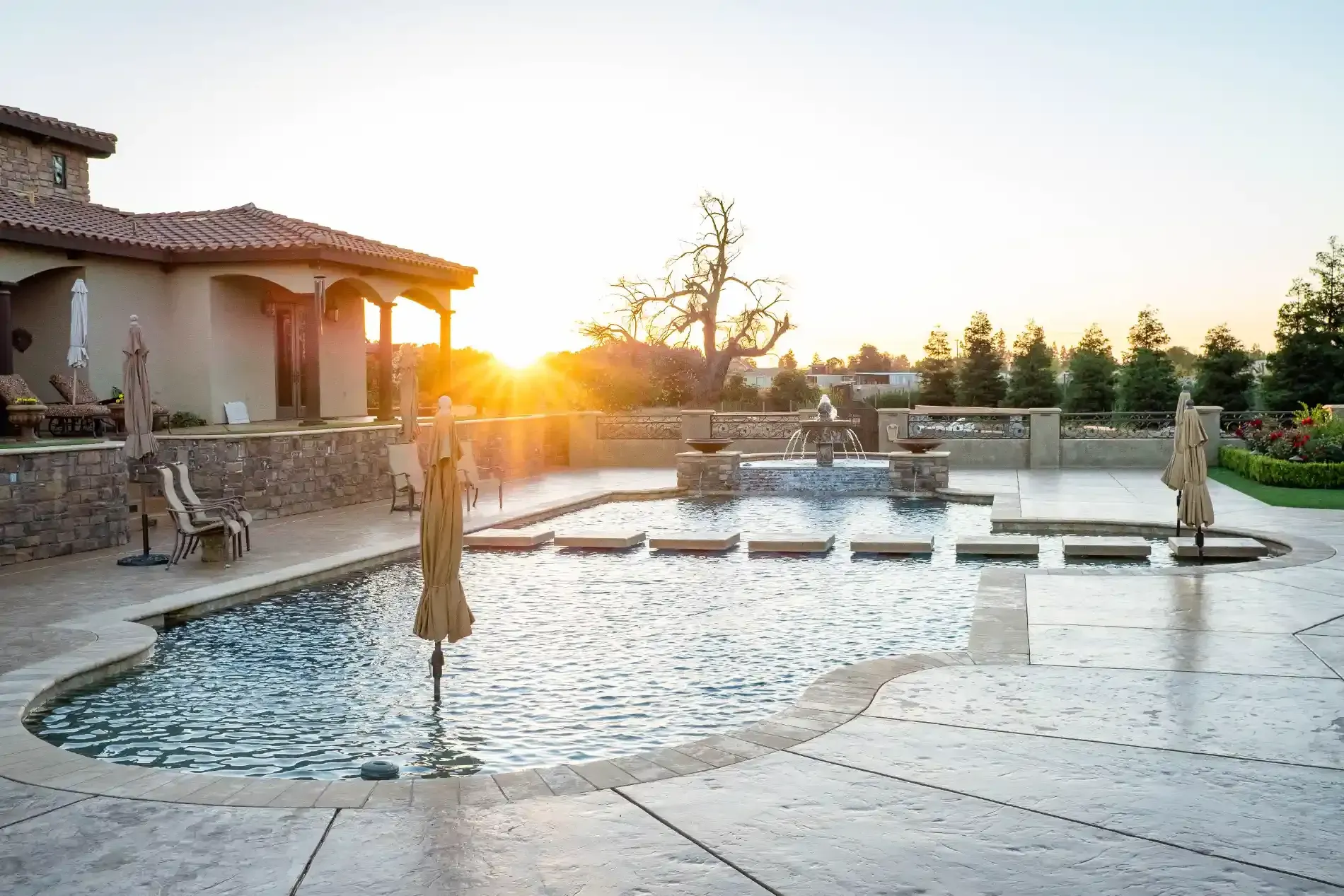 Sunlit courtyard with a reflecting pool, stone statues, and a house patio at sunset