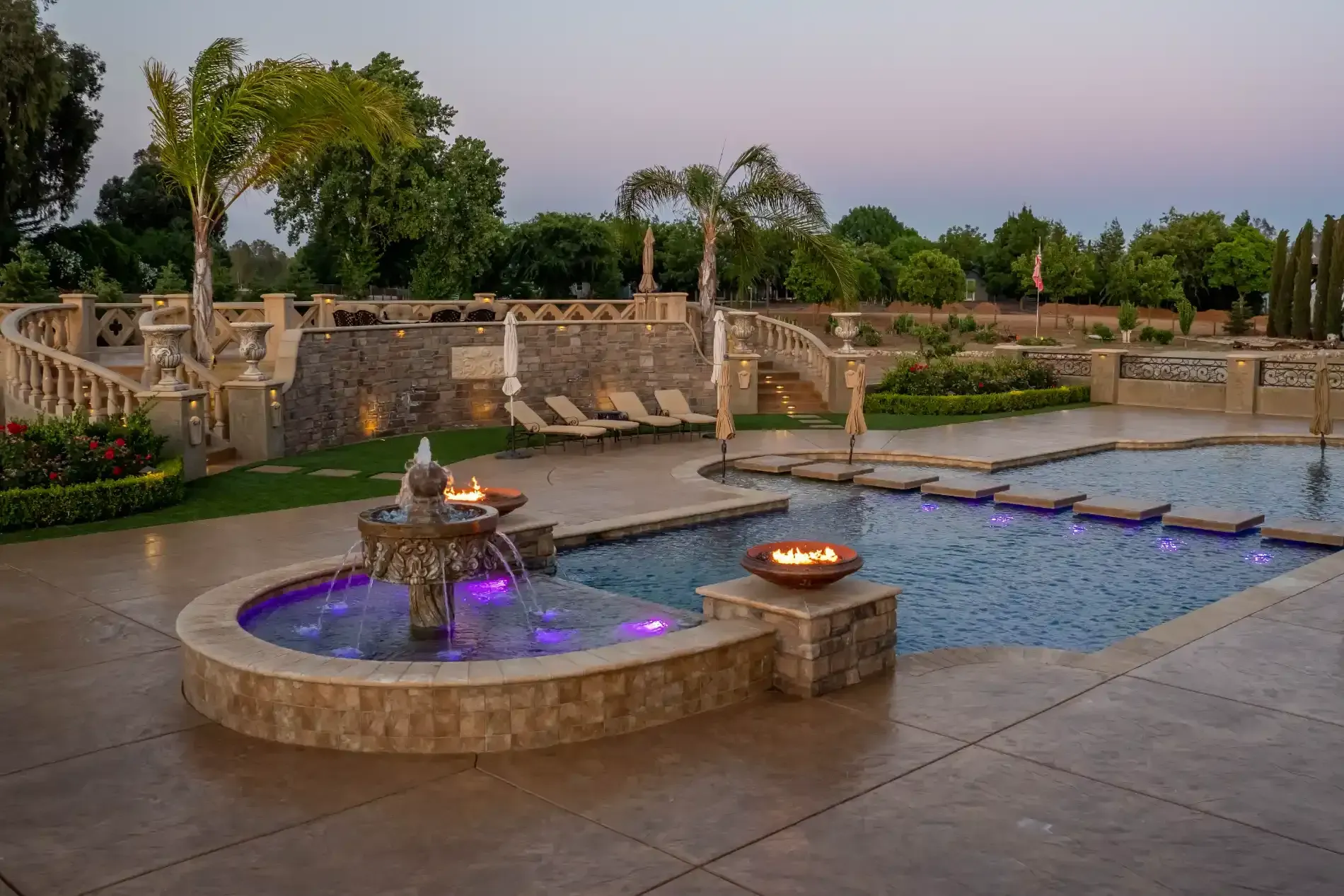 Stone fountain with purple lights beside a reflecting pool at dusk in a landscaped garden