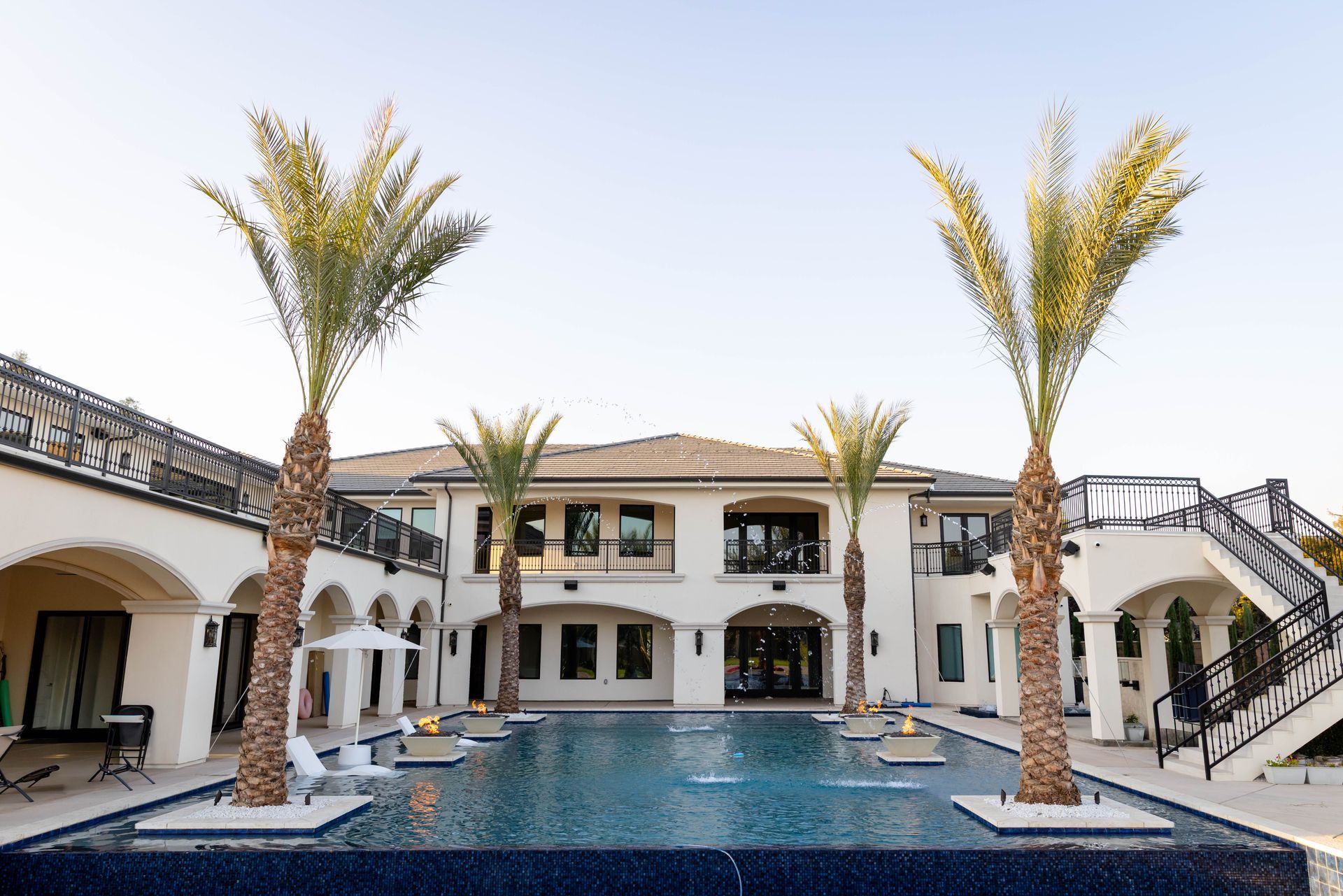 Luxury villa courtyard with a blue pool, palm trees, and white arches under a bright sky