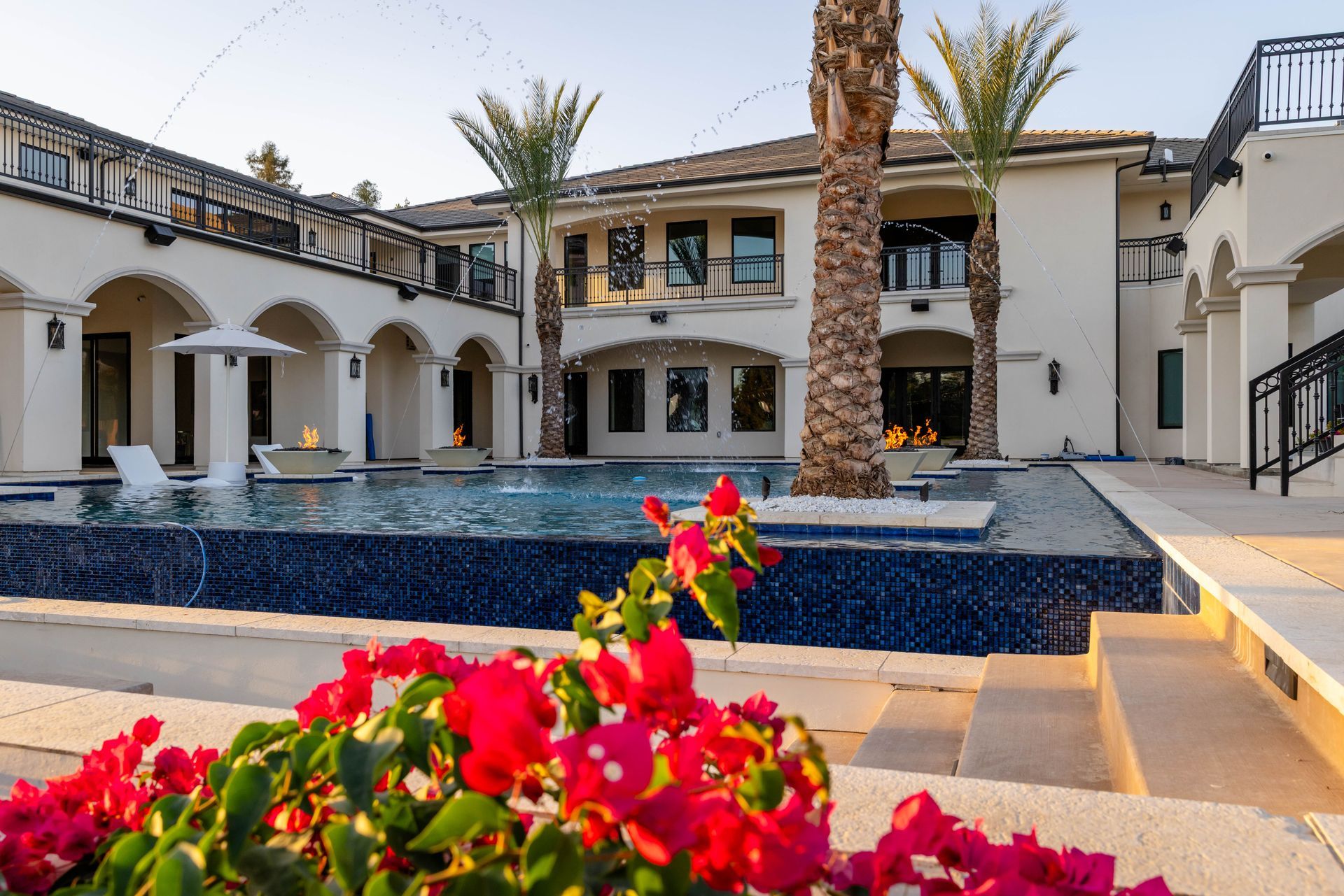 Luxury villa courtyard with blue-tiled fountain, palm trees, and bright pink flowers
