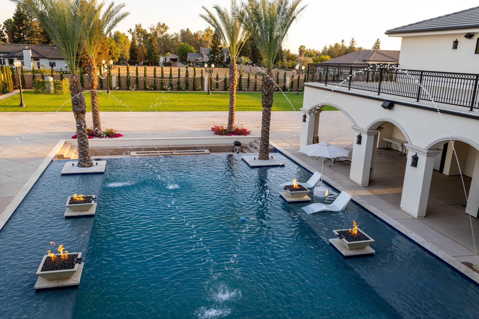 Luxury backyard pool with palm trees, loungers, and a white arched patio at sunset