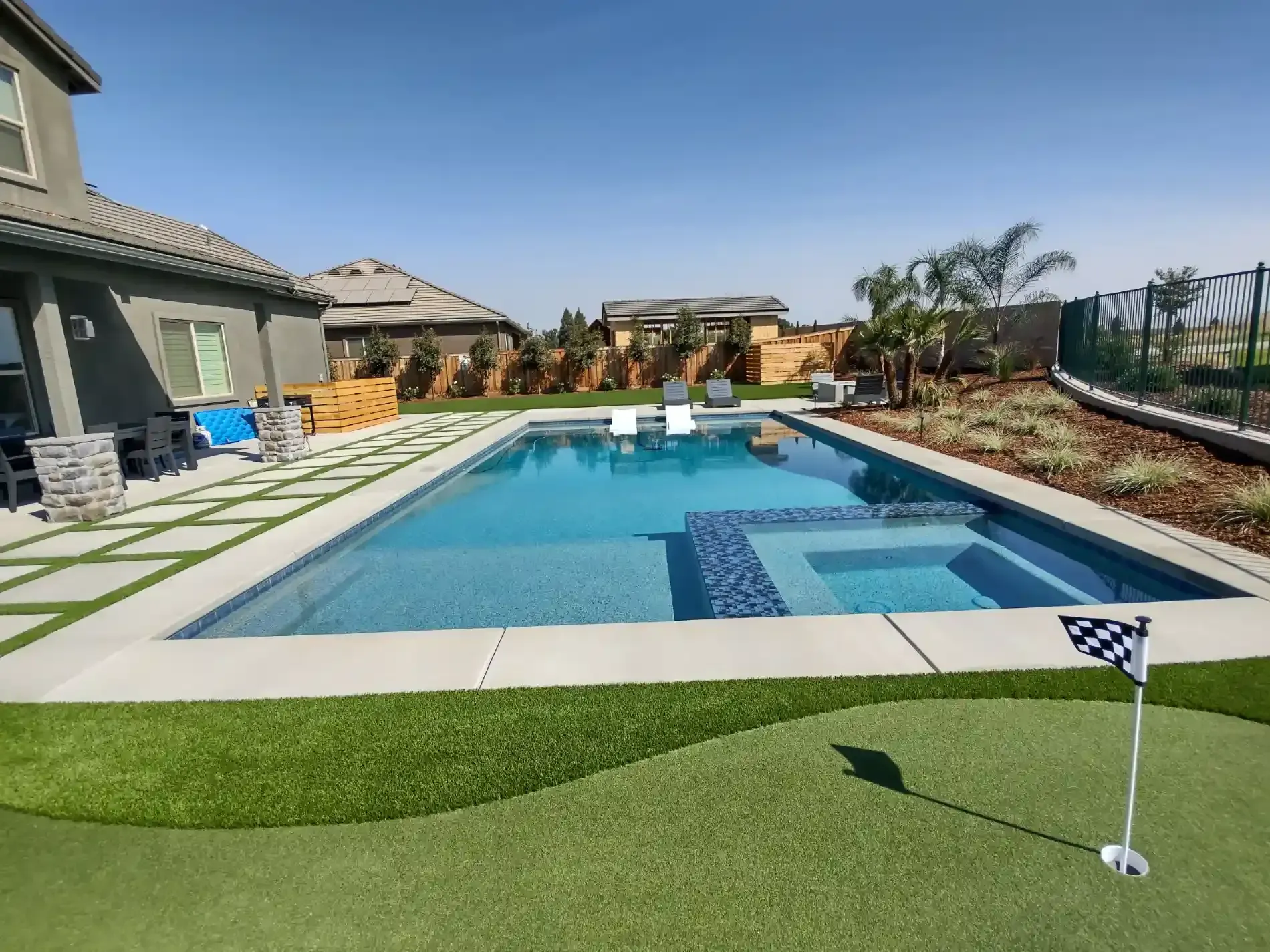 Backyard swimming pool with artificial turf, patio chairs, and a sunny sky