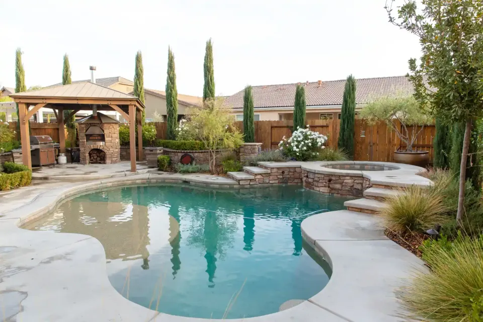 Backyard pool with stone deck, wooden pergola, and desert landscaping