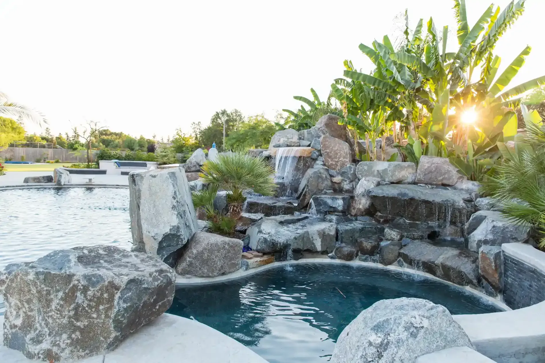Rock waterfall cascading into a blue pool in a sunlit tropical garden