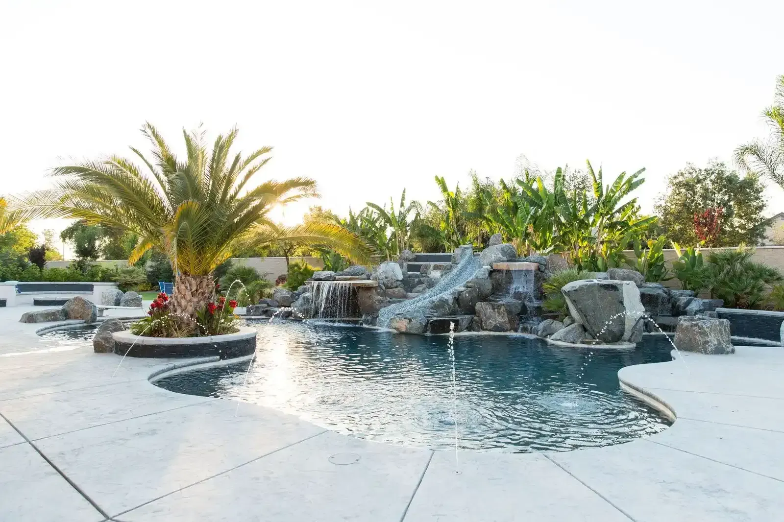 Luxury backyard pool with rock waterfall, palm trees, and sunlit patio