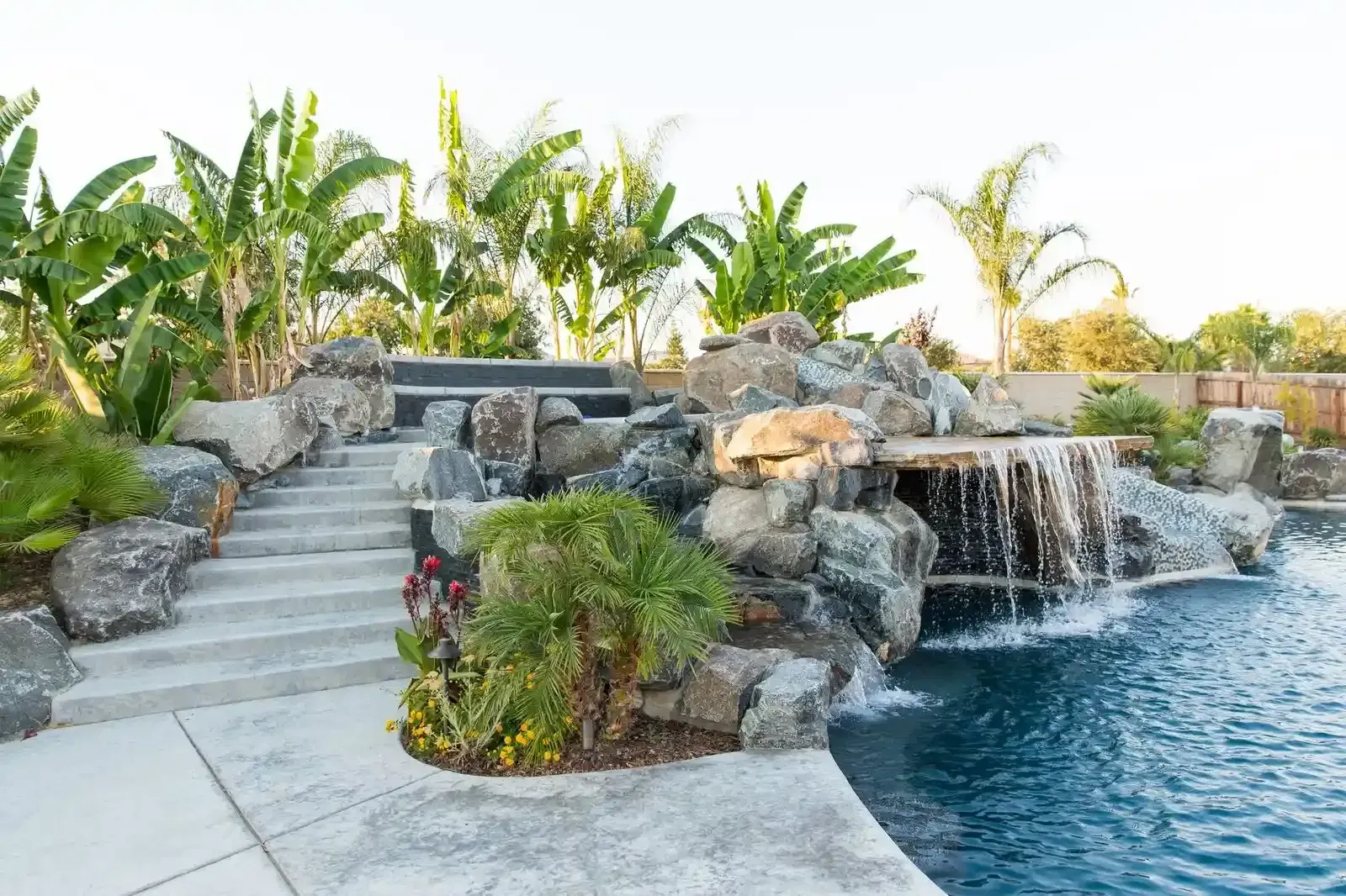 Poolside waterfall and rock garden with tropical plants and curved stone steps