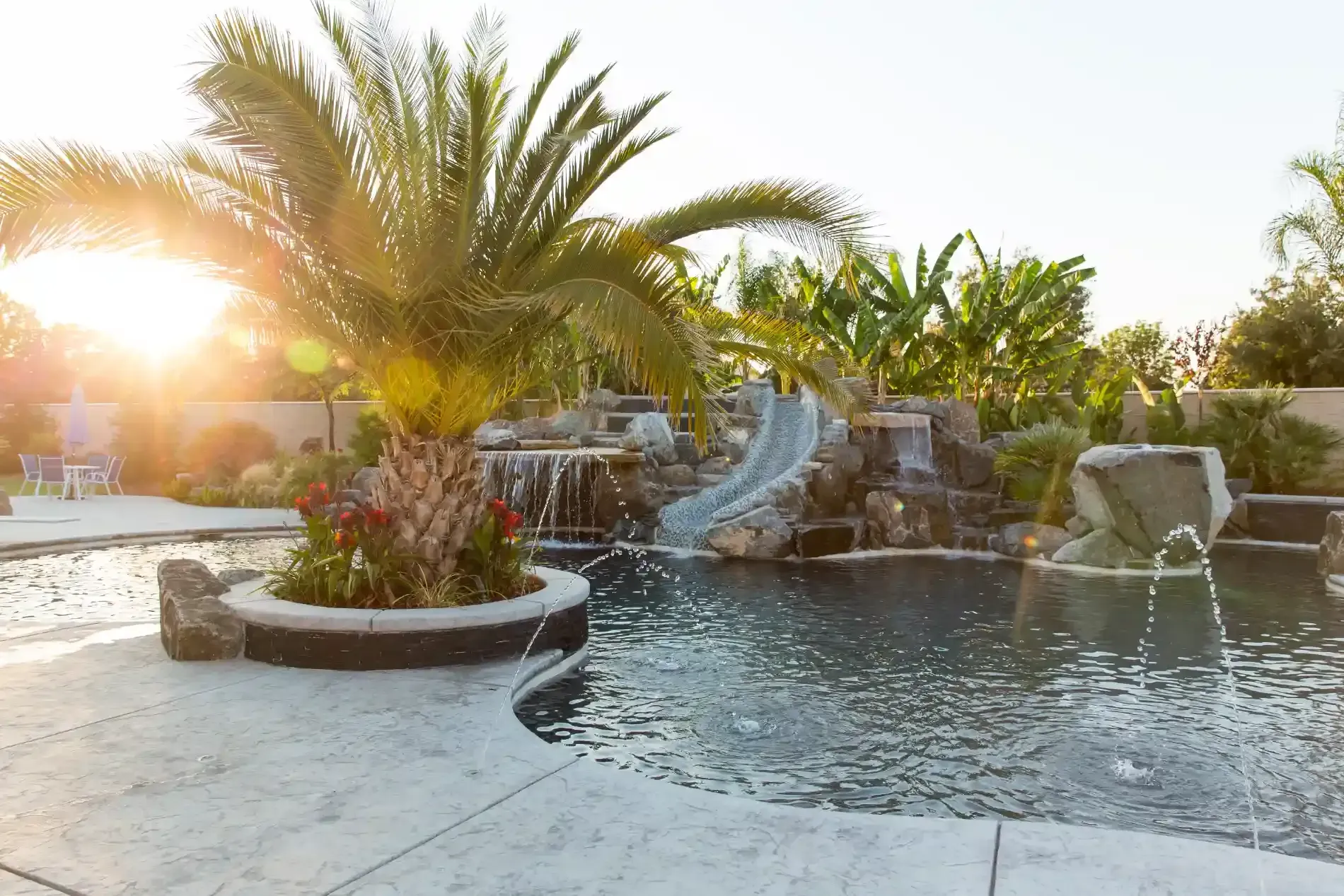Sunlit tropical resort pool with palm trees, waterfalls, and stone seating area