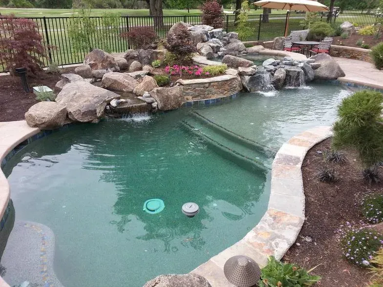 Backyard pool with a rock waterfall, turquoise water, and surrounding landscaping