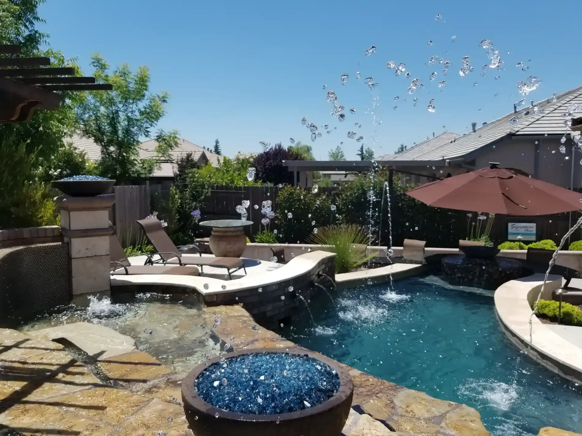 Backyard pool with waterfall, spa, lounge chairs, umbrellas, and birds flying overhead