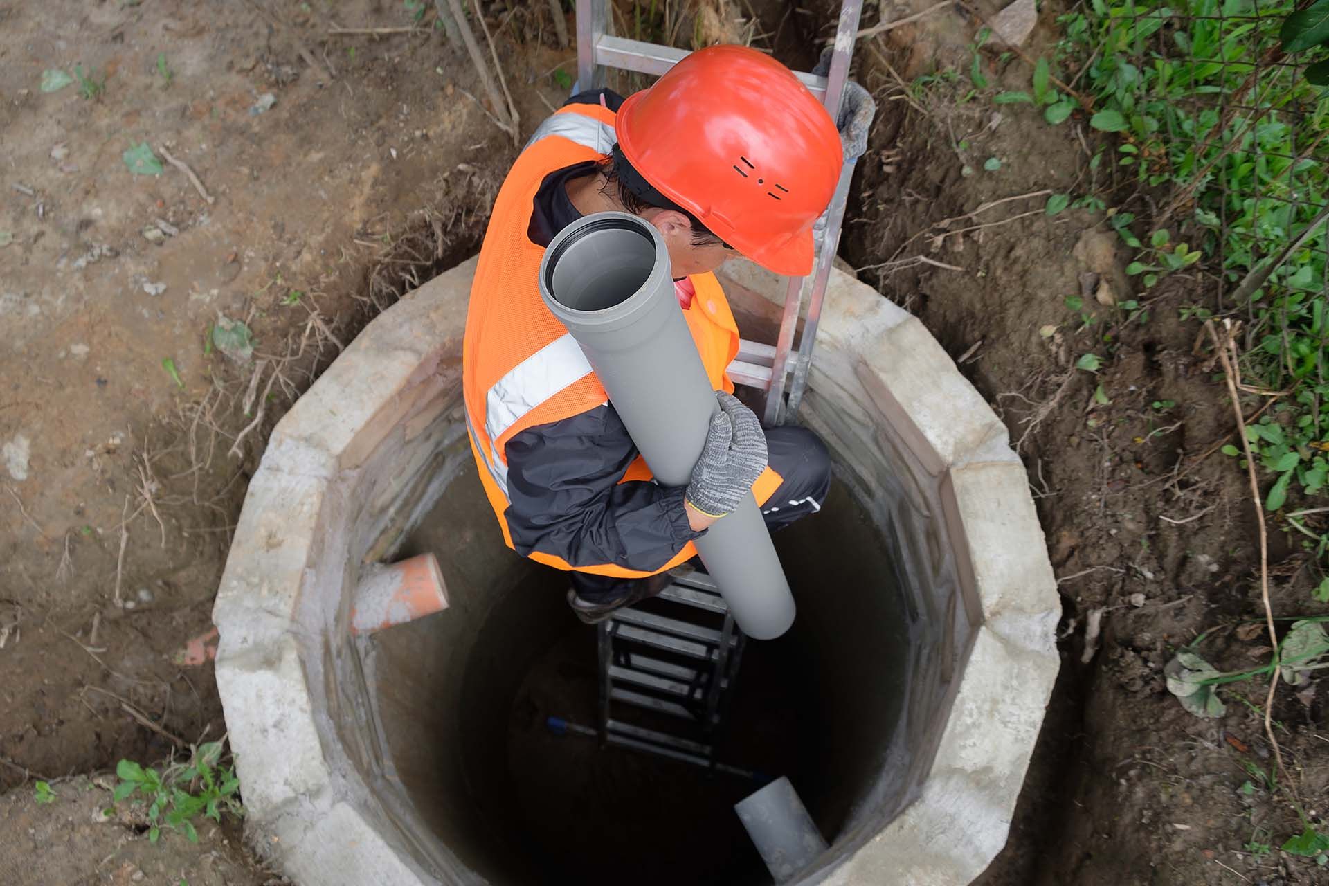 Worker performing septic system maintenance inside underground concrete septic tank.