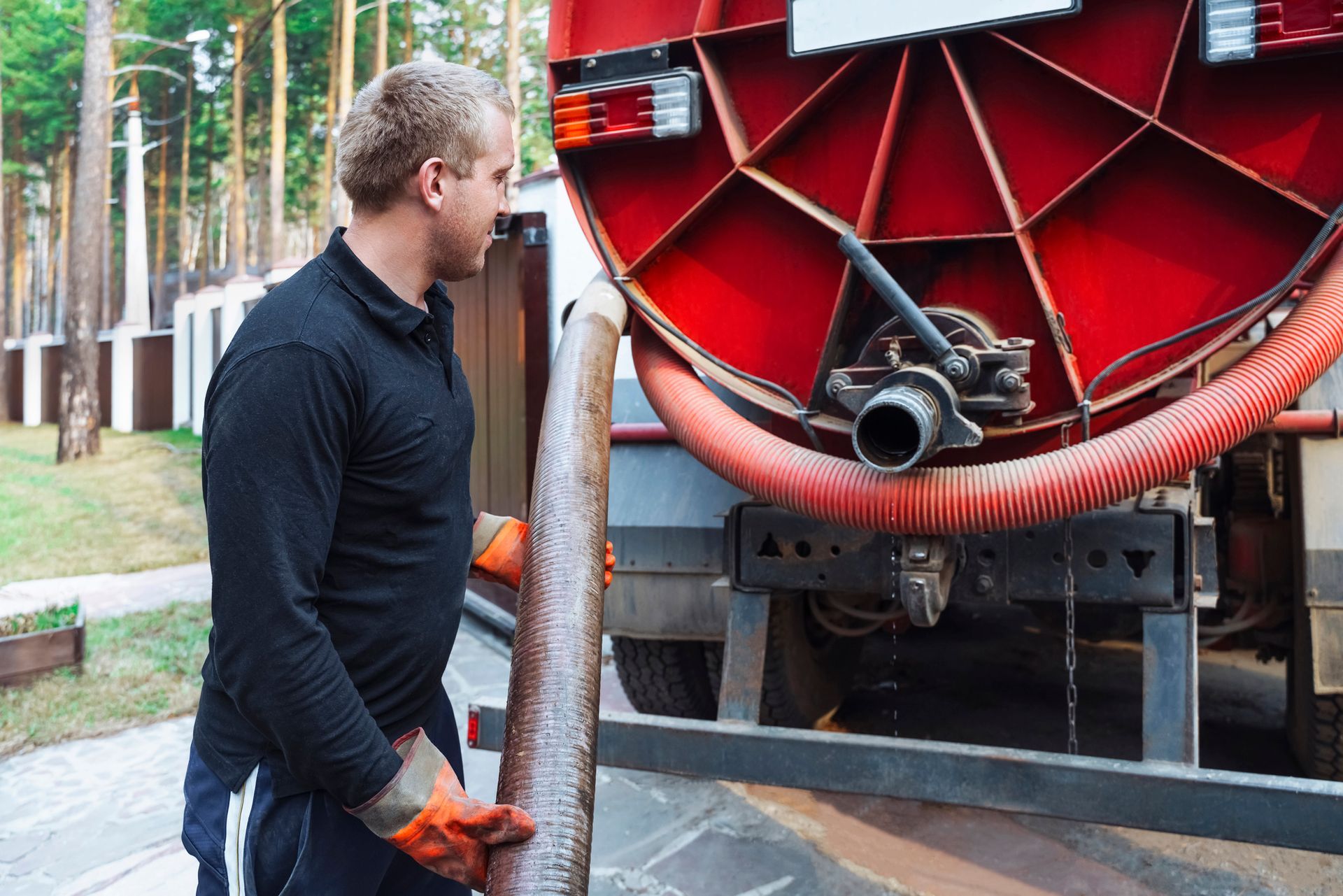 Man in orange gloves connects hose to red septic tank truck.