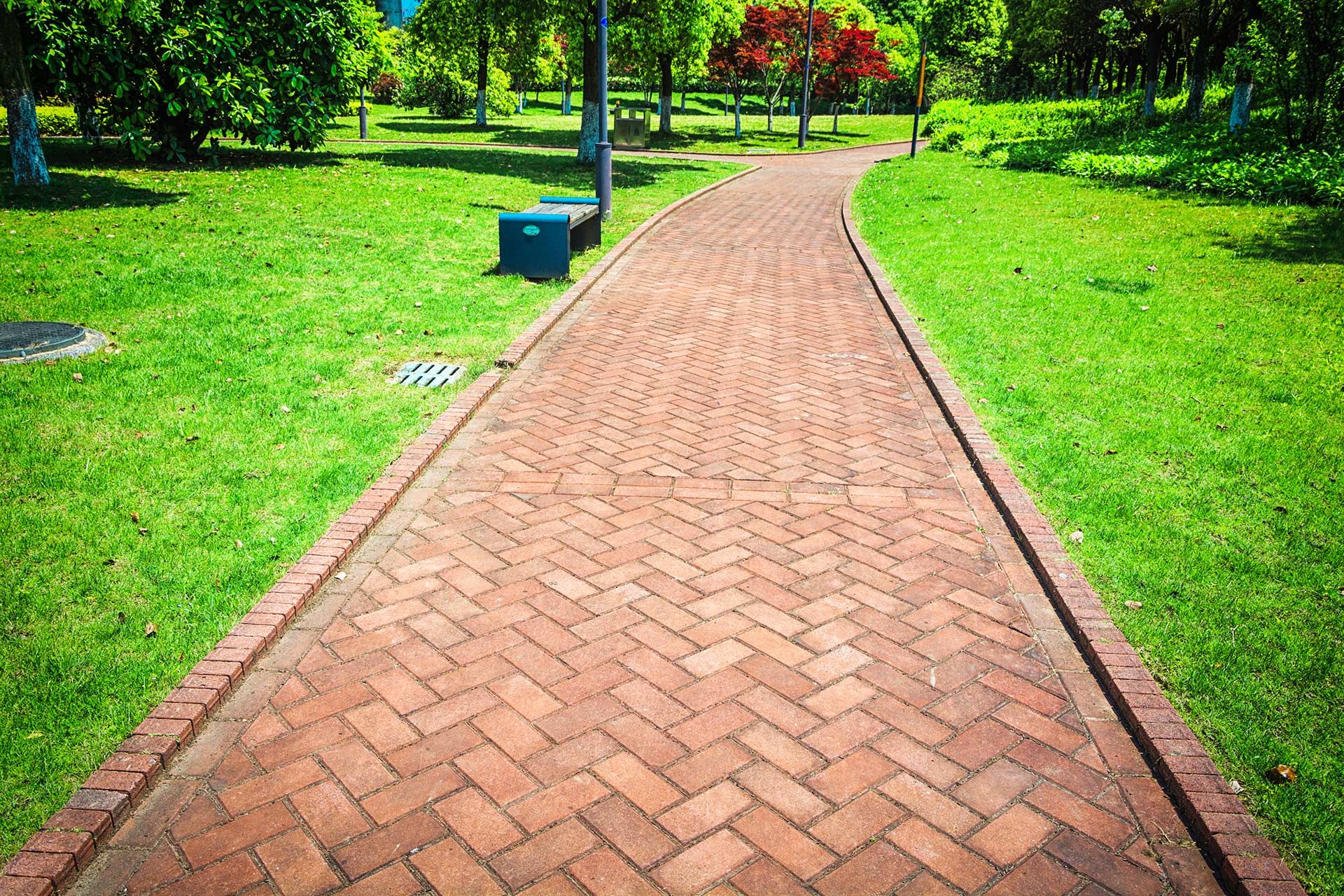 A brick walkway in a park surrounded by grass and trees.