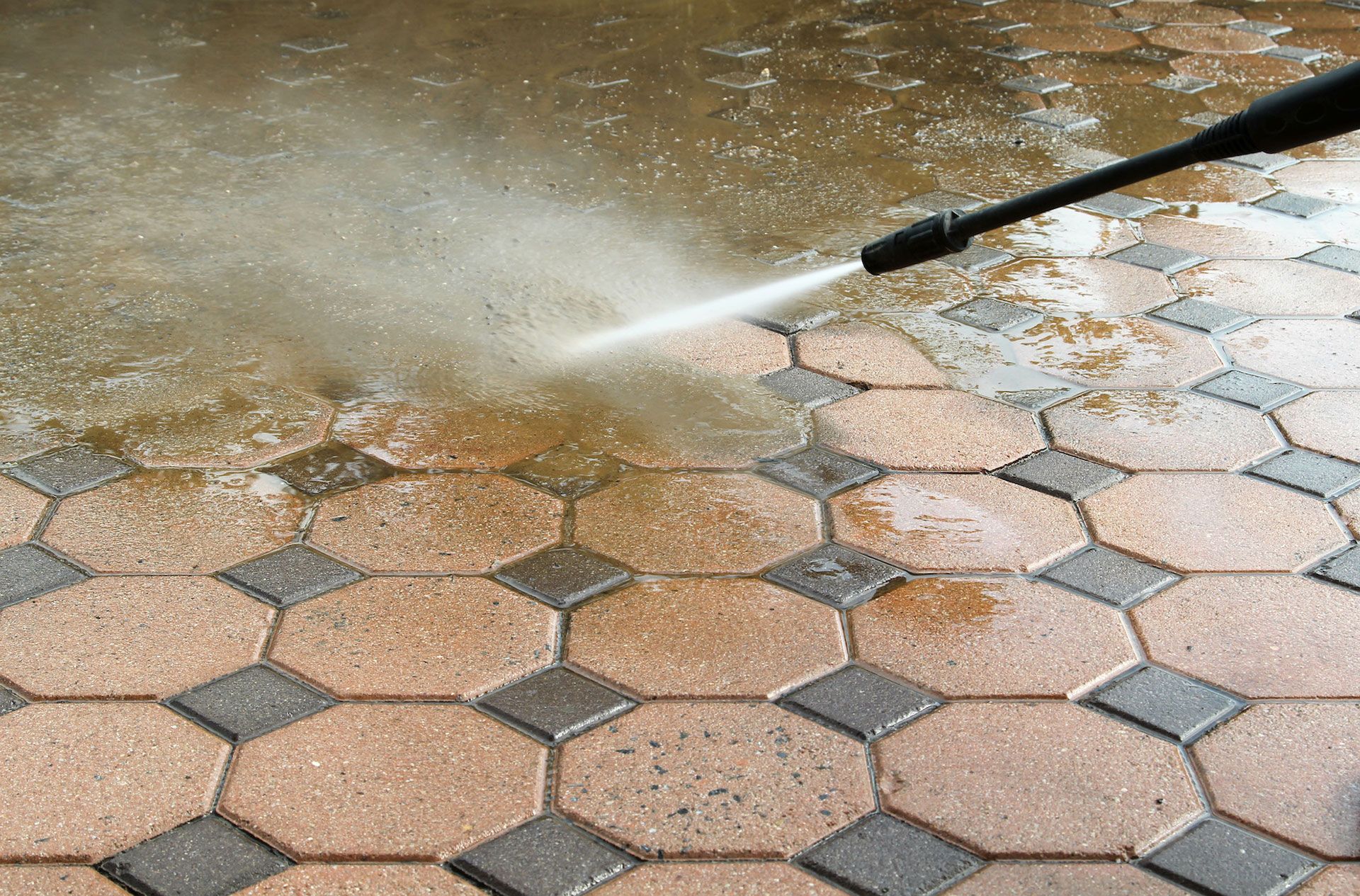 A person is using a high pressure washer to clean a brick floor.