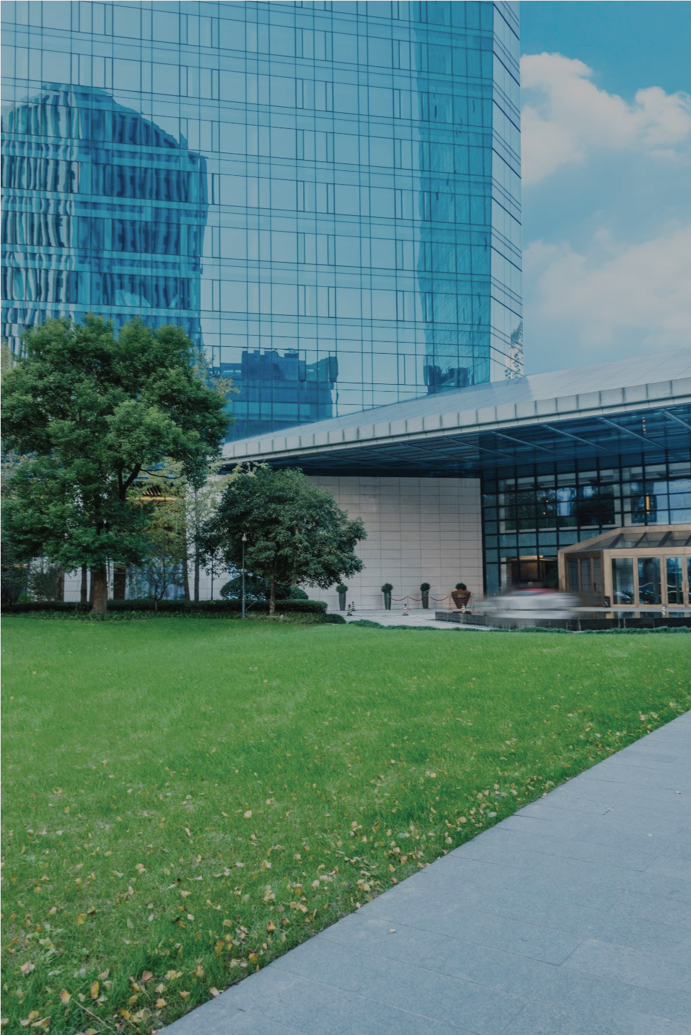 Green lawn and walkway in front of a modern glass building with a blue sky.