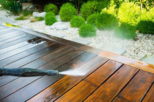 A man is using a high pressure washer to clean a brick walkway.