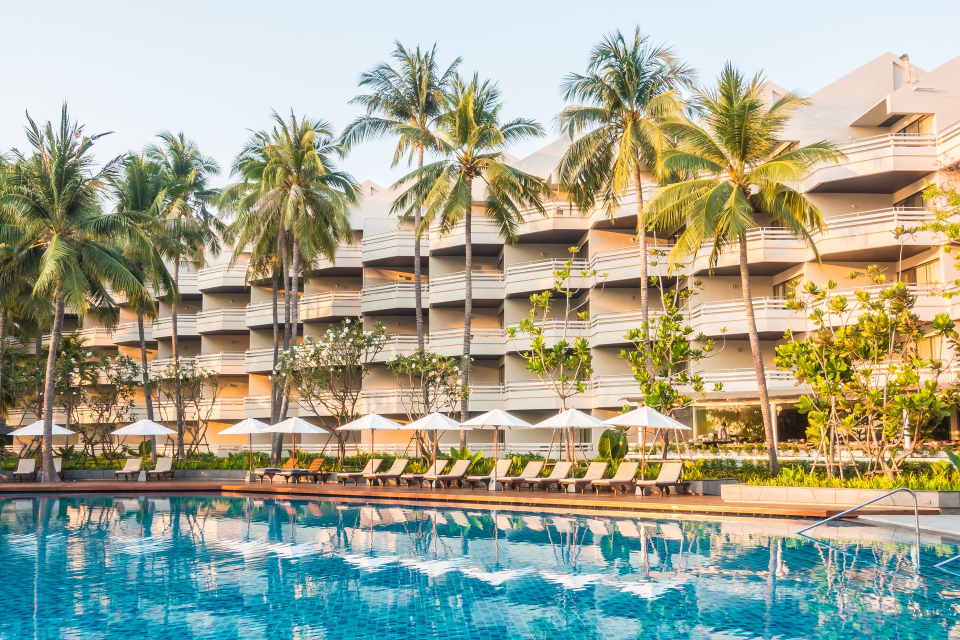 A large hotel with a swimming pool in front of it surrounded by palm trees.