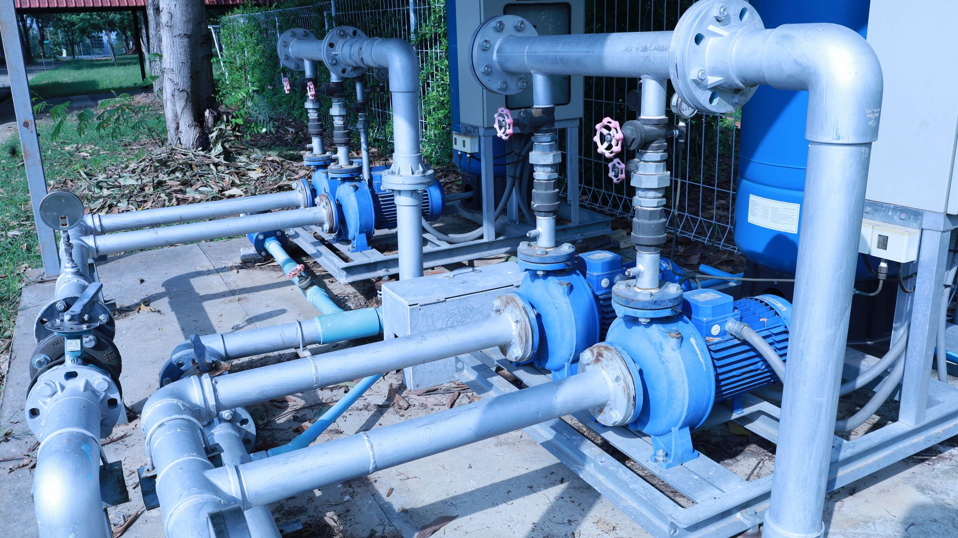 Blue water pumps with silver pipes outdoors.