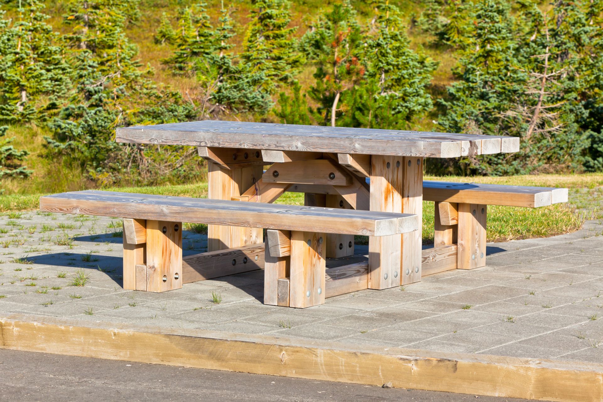 A wooden picnic table is sitting on the side of the road.
