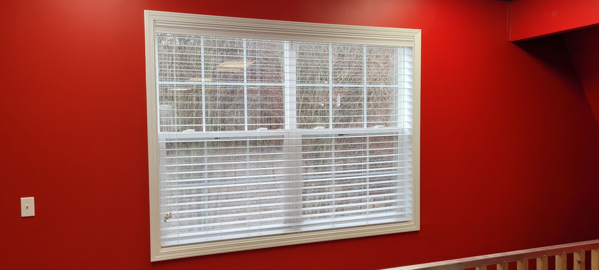 A window in a room with red walls and a wooden railing.