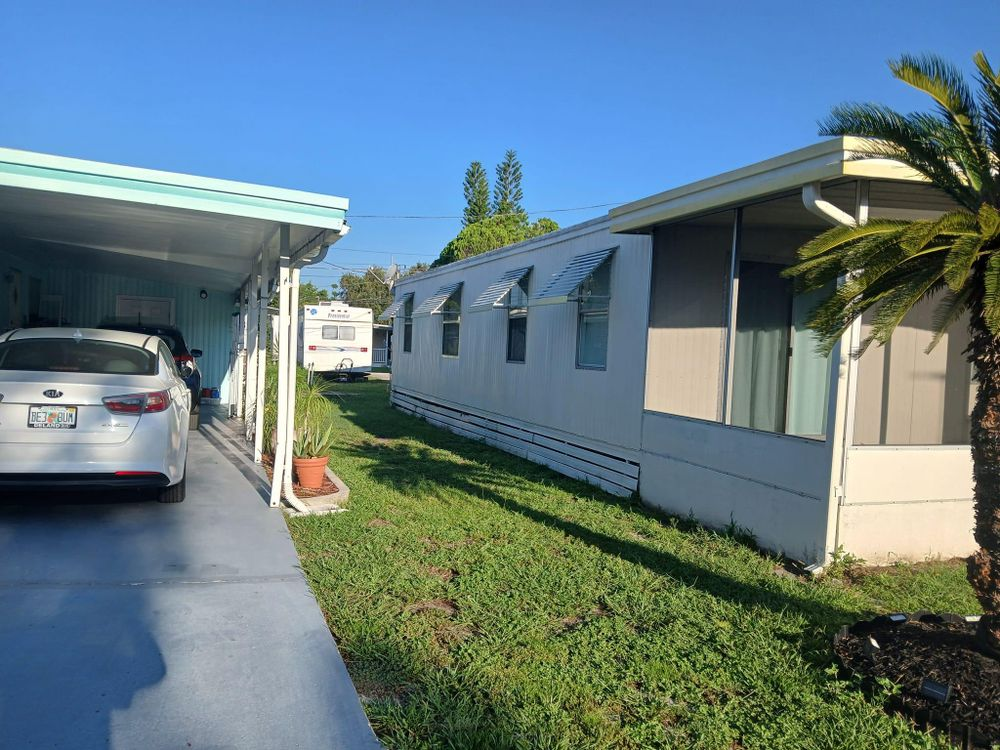 A white car is parked under a canopy in front of a mobile home