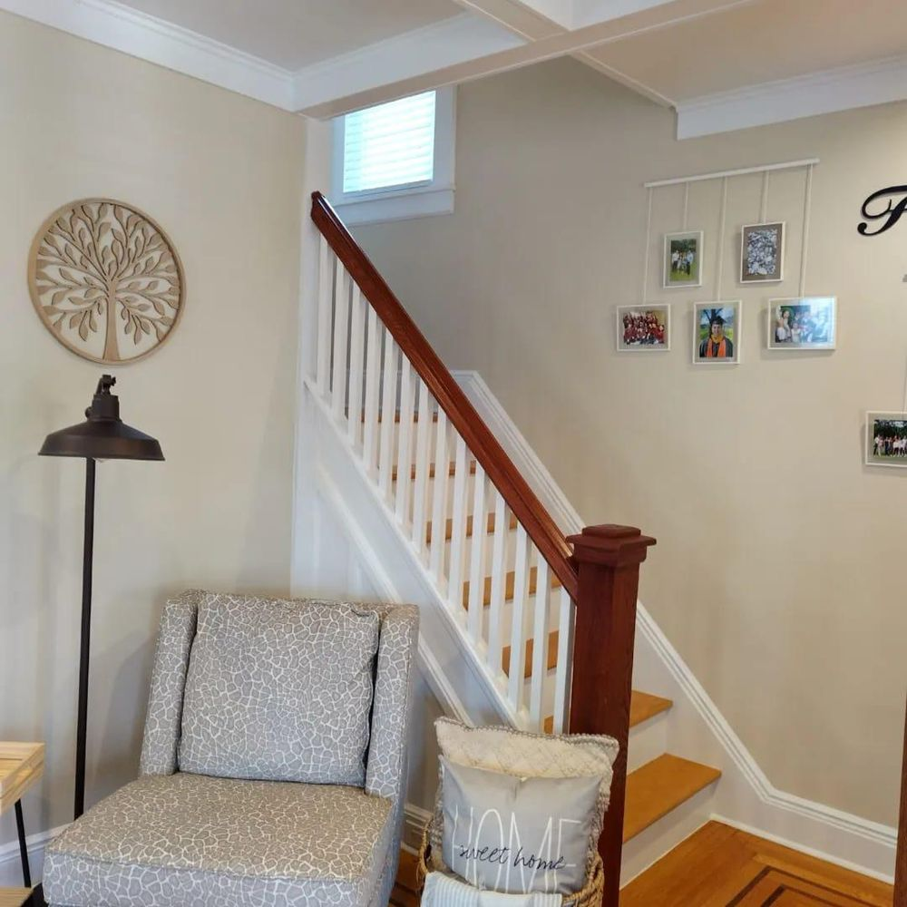 A living room with stairs and a chair and a pillow that says home