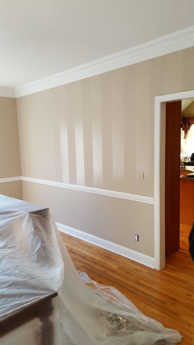 A living room with hardwood floors and beige walls is being painted.