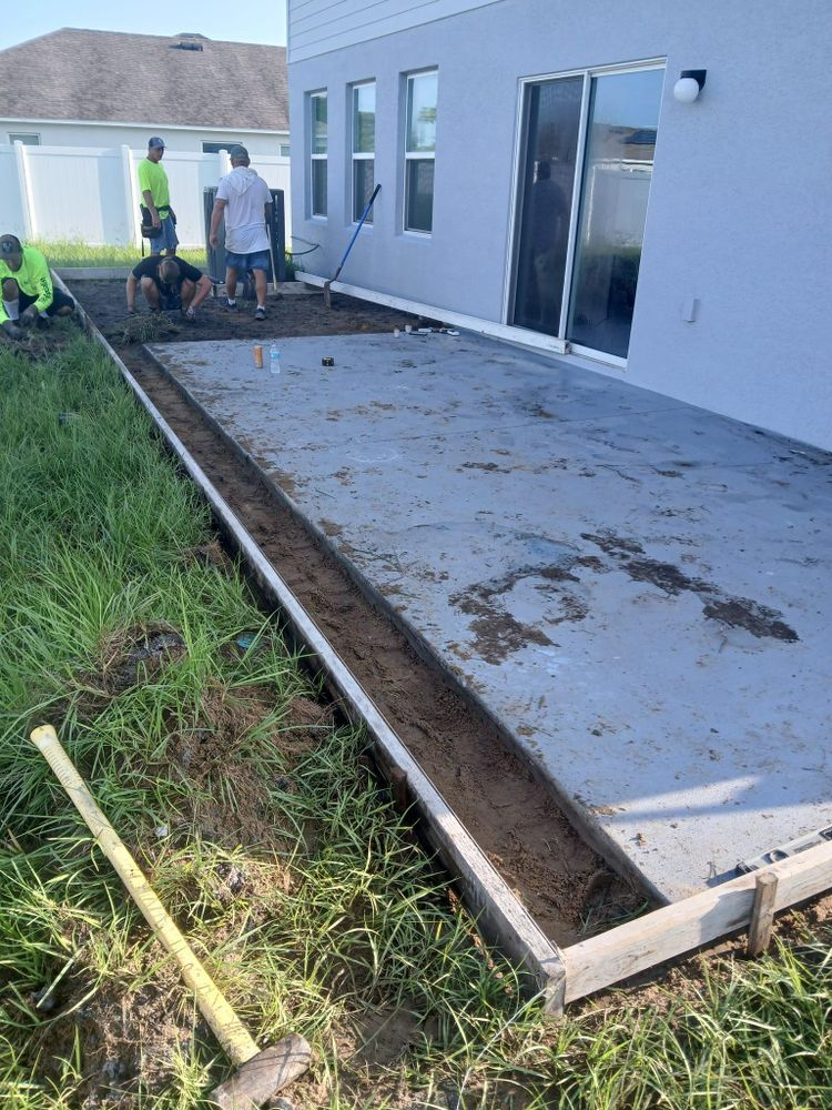 A group of people are working on a concrete patio in front of a house.