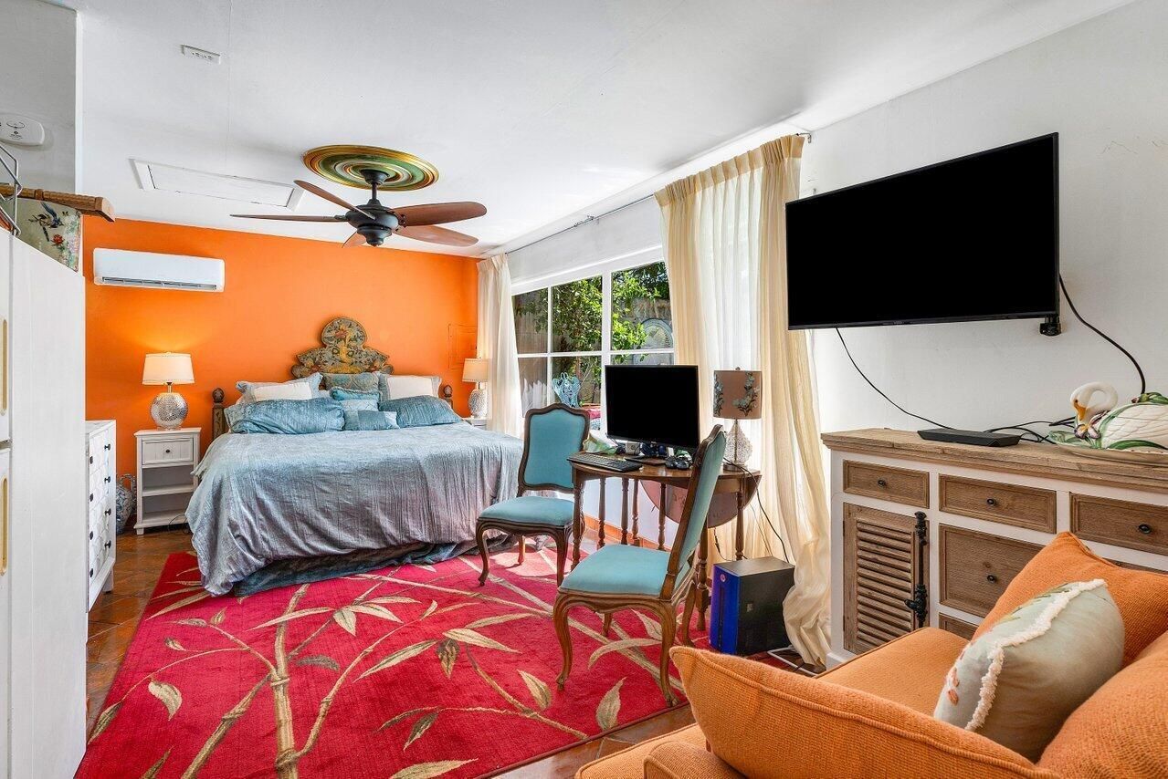 A bedroom with a large bed , chairs , a television and a ceiling fan.