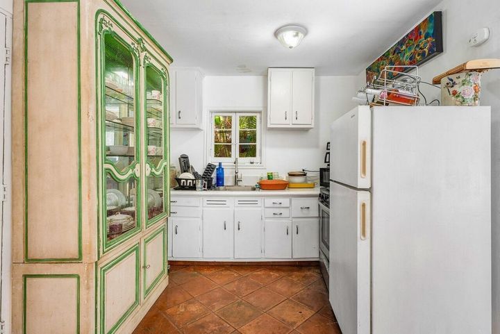 A kitchen with white cabinets , a refrigerator , a sink , and a hutch.