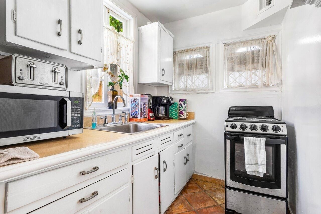 A kitchen with white cabinets , a stove , microwave and sink.