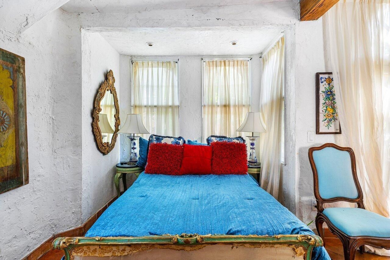A bedroom with a bed , chair , mirror and paintings on the wall.