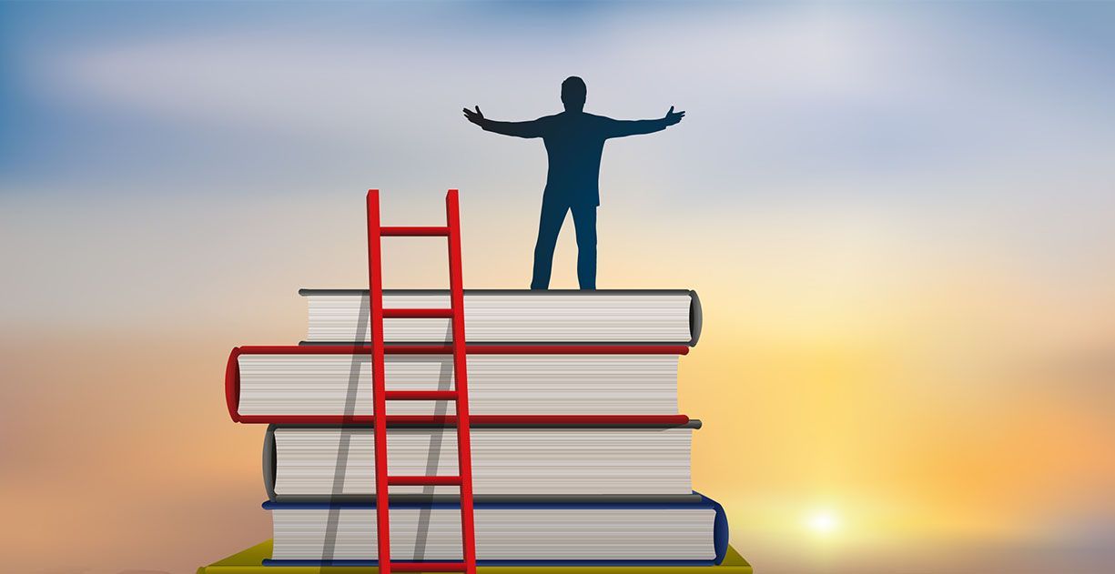 A silhouette of a person standing with arms outstretched on a stack of four books beside a red ladder at sunset.