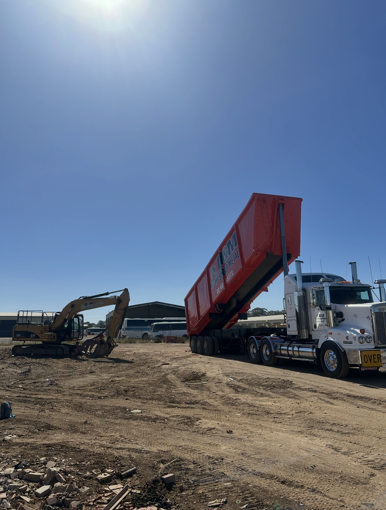 A yellow excavator next to a white truck with the back trailer on an angle.