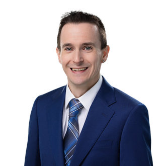 Man in a blue suit, glasses, and a patterned tie, smiling. Studio shot.
