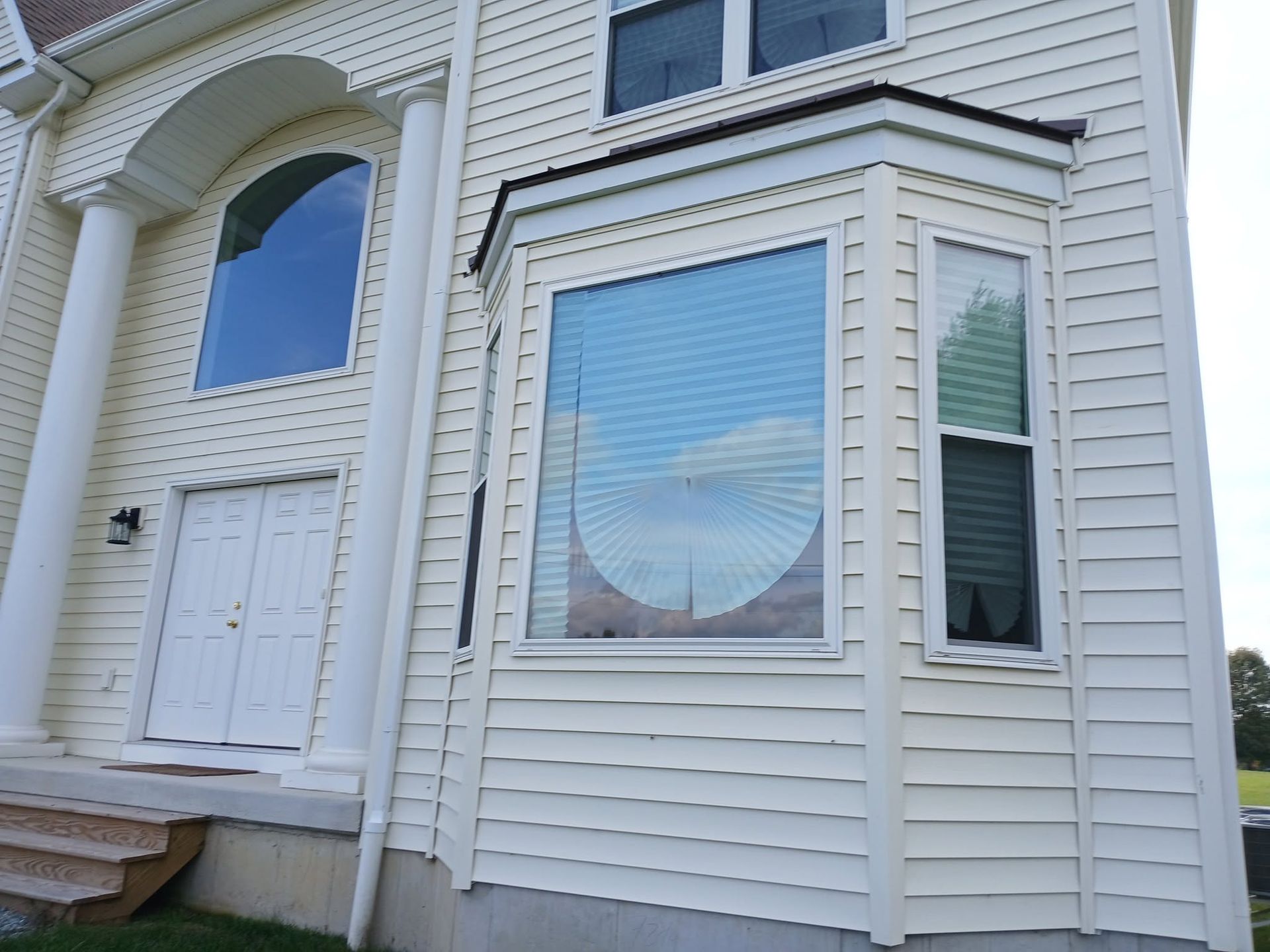 Exterior of a white house with a front door, large windows, and vinyl siding under a clear sky