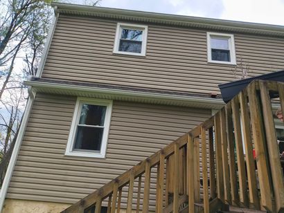 Two-story tan house with white-trimmed windows and a wooden staircase railing in the foreground