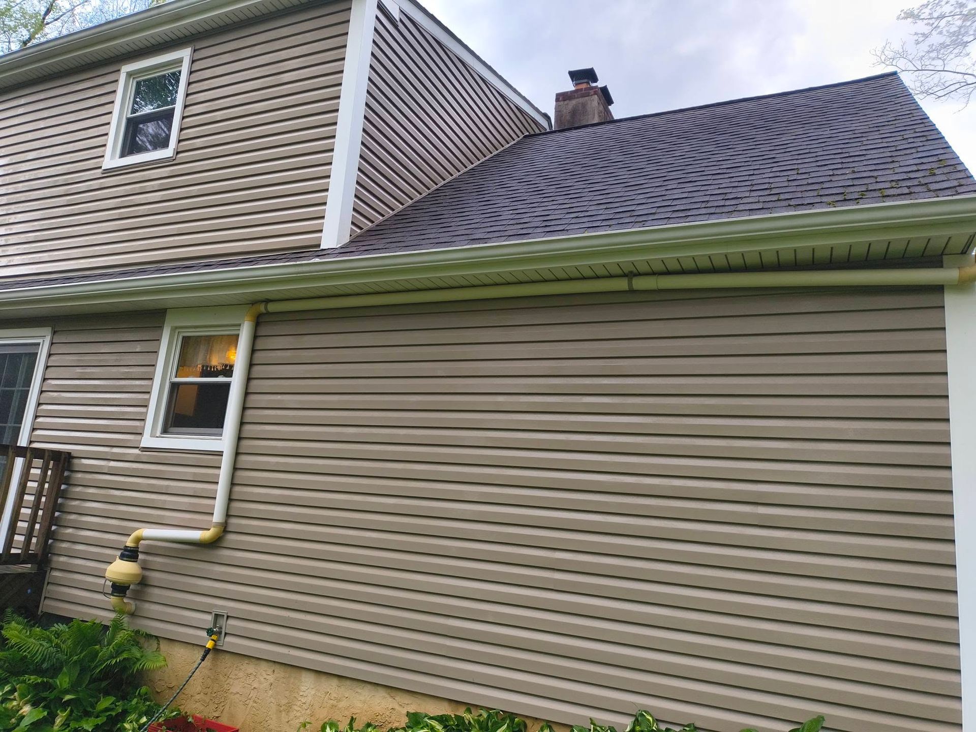Side view of a beige house with vinyl siding, roof shingles, and a downspout on the exterior wall