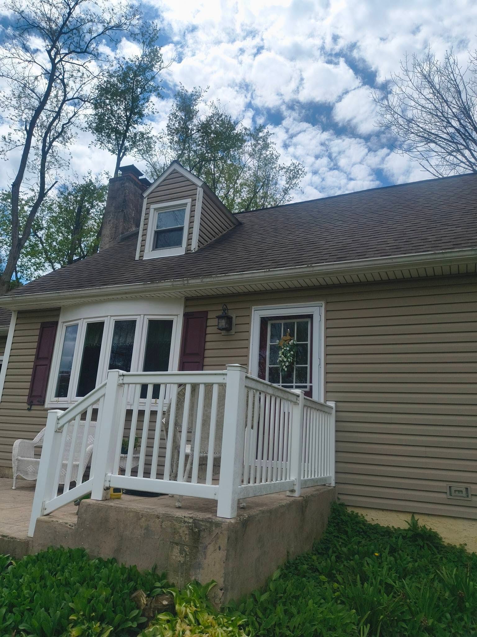 Small house with white porch railing, beige siding, and a cloudy sky overhead