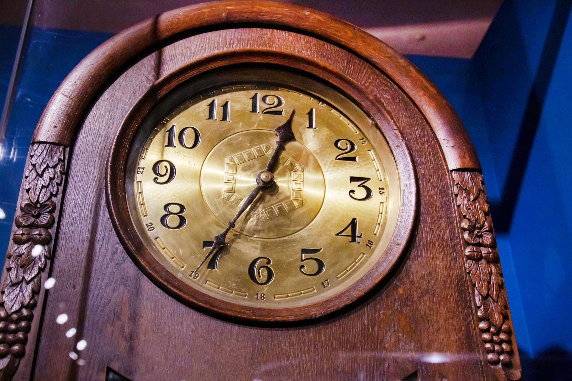 The gold-colored dial of an antique wooden grandfather clock with hands.