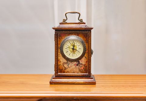 A man's hand winding a grandfather clock Ornate vintage clock on a wooden table against a plain gray background.