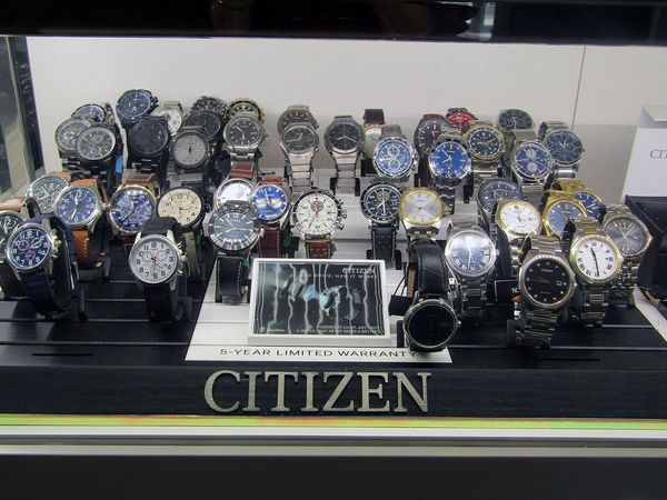 Display of Citizen watches on a black surface, many with silver and blue faces, in a store setting.