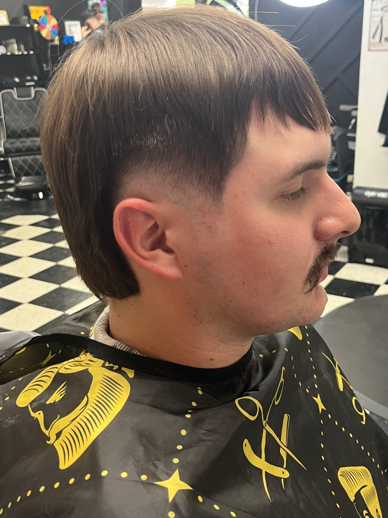 Man with a mullet hairstyle, faded sides, and mustache in a barber shop.