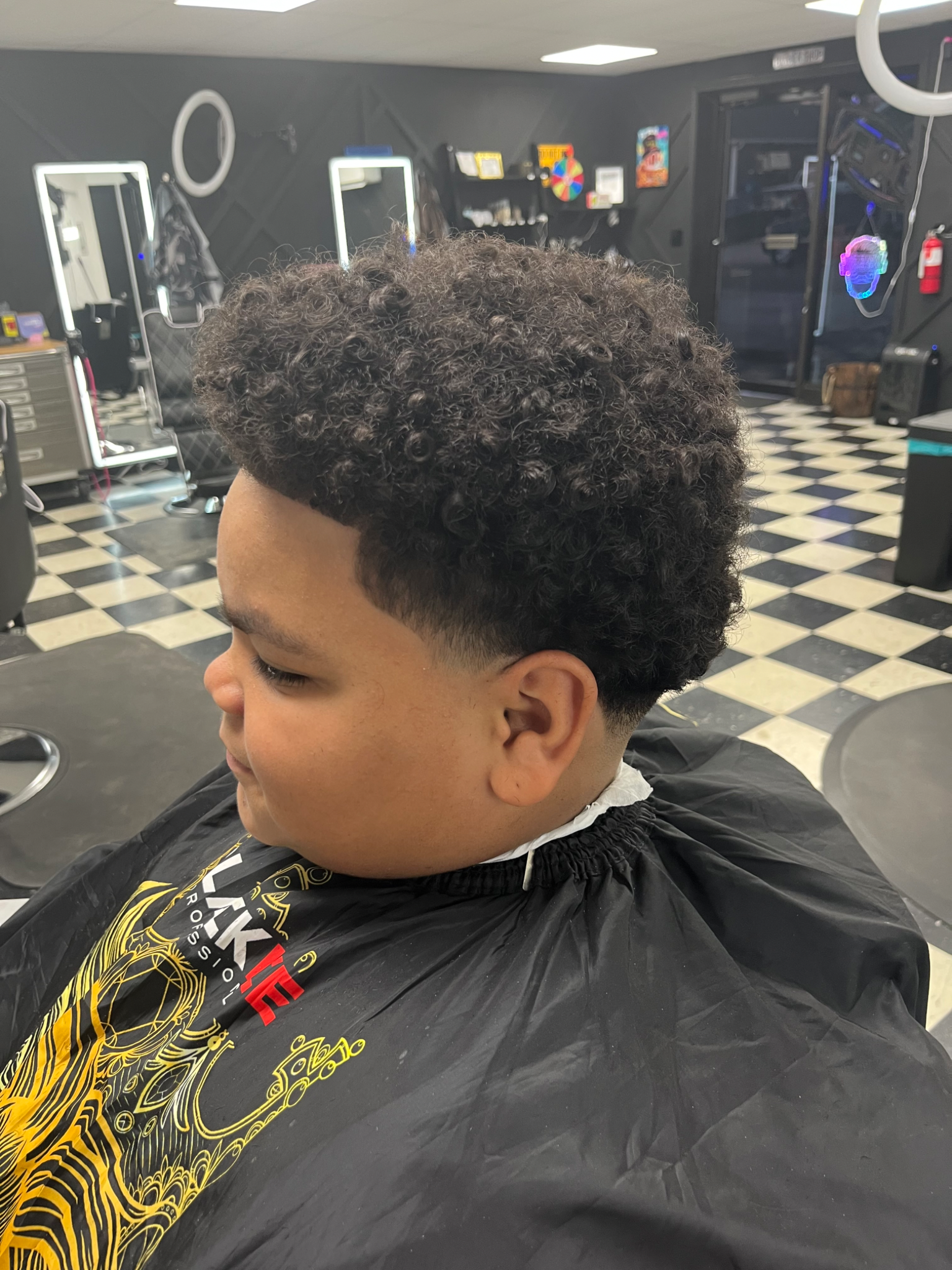 Boy with dark curly hair and a fade haircut at a barbershop.