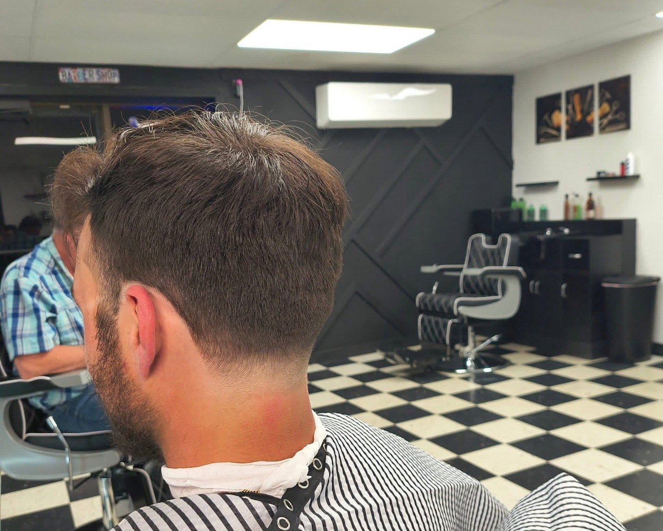 Man getting a haircut in a barbershop. Fade haircut, black and white checkered floor, barber chair, and black accent wall.