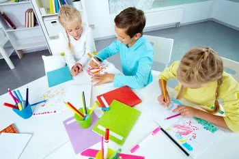 Children drawing at a table with colored pencils and paper in a bright classroom