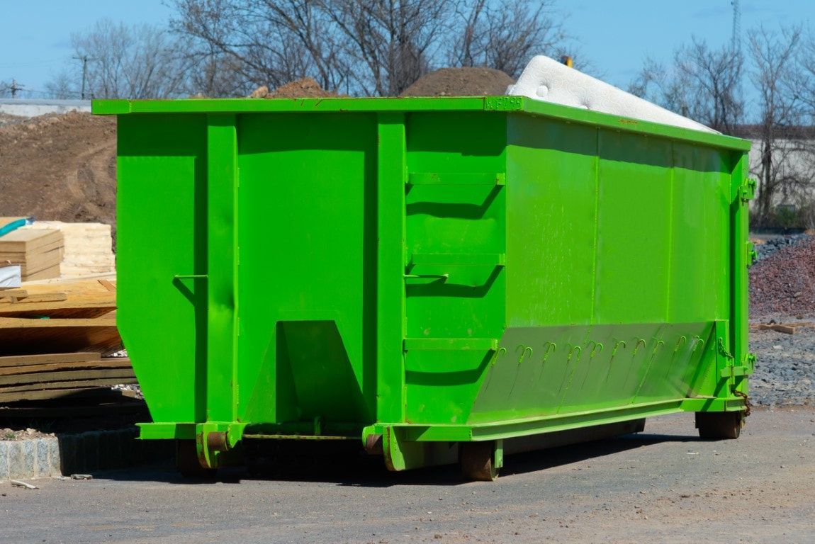 Green dumpster on wheels, outdoors, containing white debris.