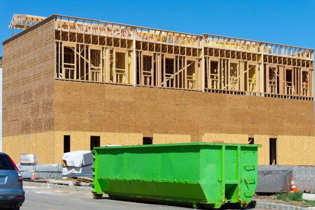 Green dumpster in front of a building under construction; wooden framing visible.